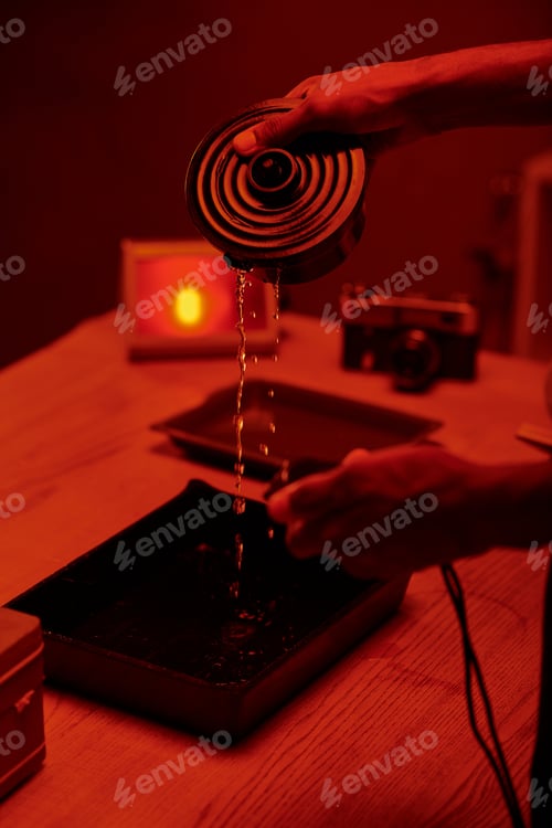 Preview: cropped photo of photographer pouring developer liquid for film processing, red darkroom