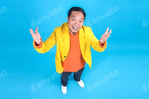 Preview: Funny Young Asian Man in Trendy Yellow Suit Standing While Posing Isolated on Blue Background
