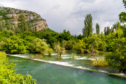 Preview: Tranquil river flowing through a lush landscape with overcast skies and towering cliffs