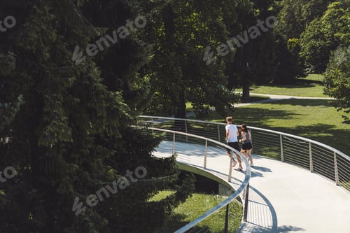 Preview: A couple walking hand in hand on a curved pathway in a lush green park. The scene is bright and sunn