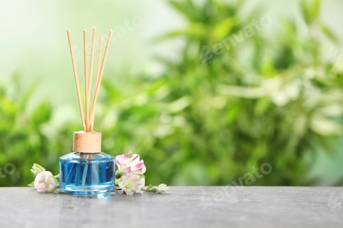 Preview: Reed air freshener and flowers on grey table against blurred green background. Space for text