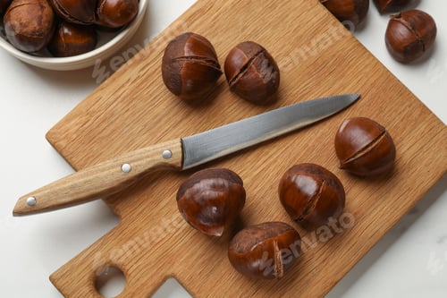 Preview: Roasted edible sweet chestnuts and knife on white table, flat lay