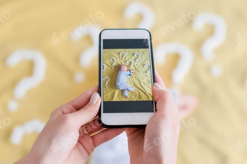 Preview: cropped shot of mother taking top view photo of adorable child sleeping in bed surrounded with