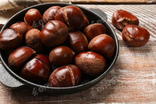 Preview: Fresh edible sweet chestnuts in frying pan on wooden table, closeup