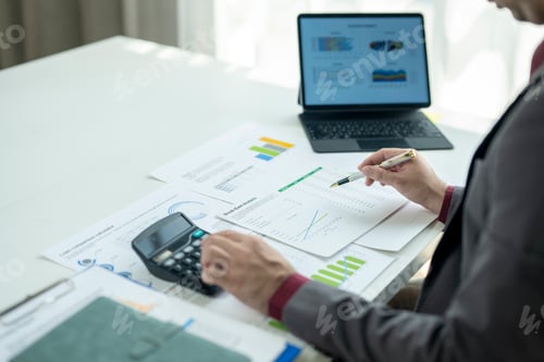 Preview: A man is working on a spreadsheet with a calculator and a pen