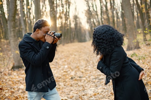 Preview: Black man take a photo of black woman in autumn park