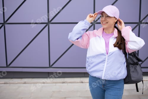 Preview: Woman smiling with white teeth, adjusting her cap against the background of the wall