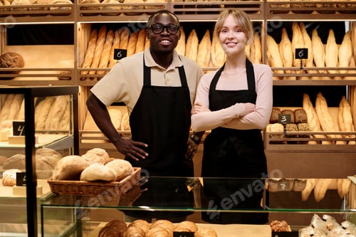 Preview: Two young people in artisan bakery standing behind counter and smiling at camera