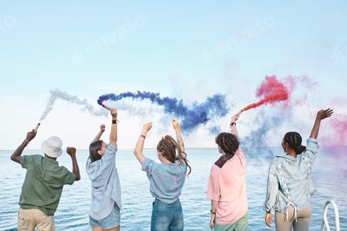 Preview: Five ecstatic friends with colorful firecrackers having fun by waterside