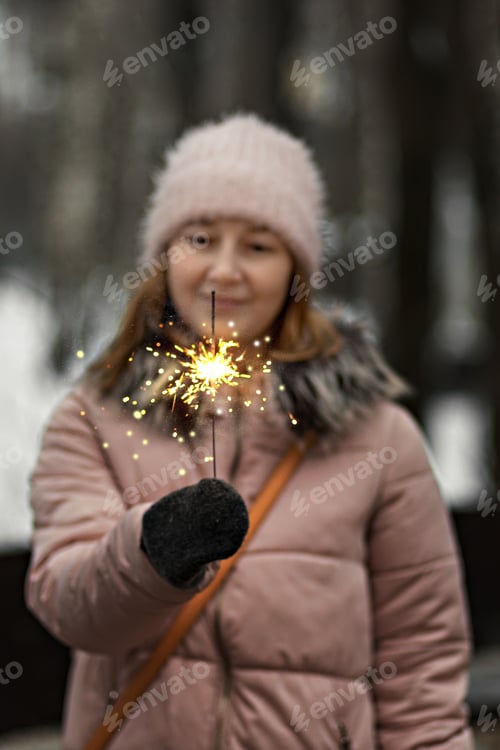 Preview: Christmas lights are bright splashes burning in the hands of a blurry happy woman in the park.