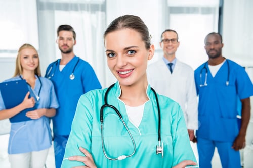 Preview: young attractive nurse with crossed arms with colleagues standing together on background