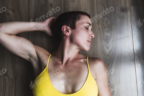Preview: Athletic Caucasian female wearing a yellow gym outfit lying on a wooden surface