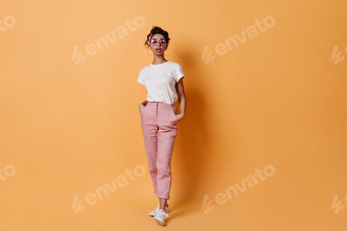 Preview: Full length view of curious girl in pink pants. Studio shot of interested mixed race woman posing w