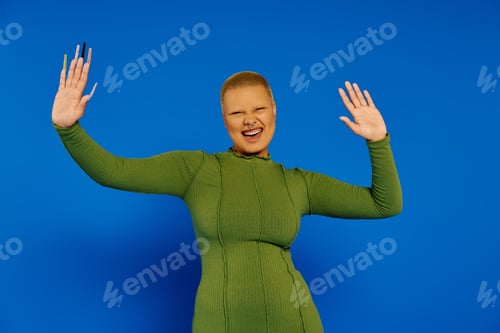 Preview: A joyful young woman in a green outfit against a vibrant blue background celebrating her style