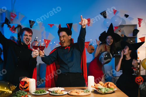 Preview: Four friends dressed as witches and devils celebrate Halloween, raising glasses of red wine