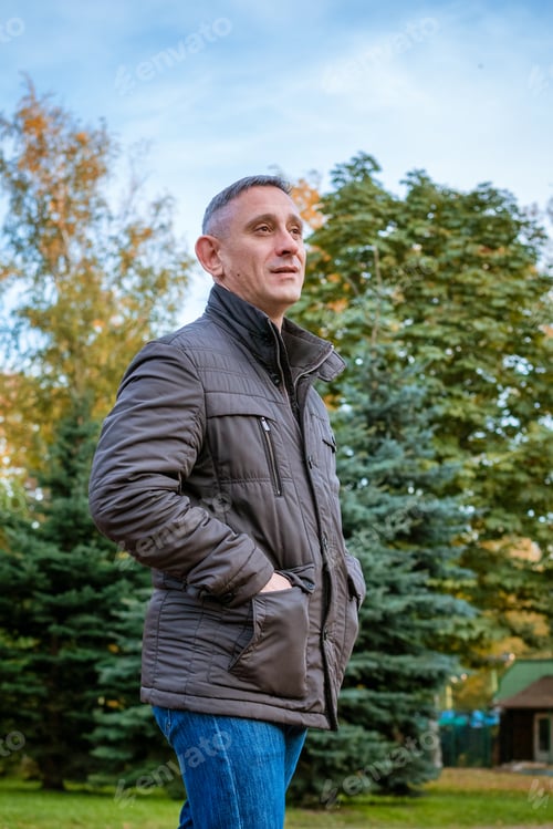 Preview: a man in an autumn jacket in the park stands on the path