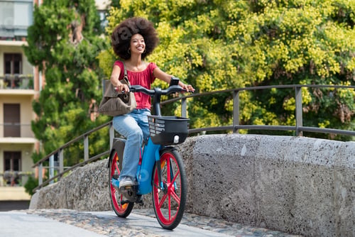 Preview: Happy black woman riding electric bicycle on city street bridge