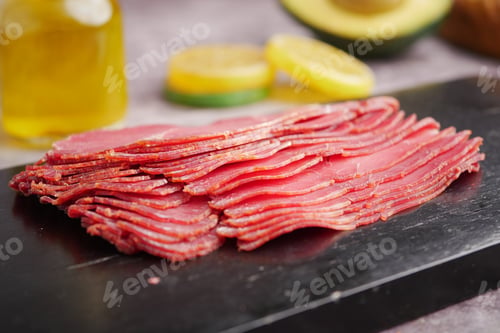 Preview: Sliced meat on a dark board with fresh ingredients