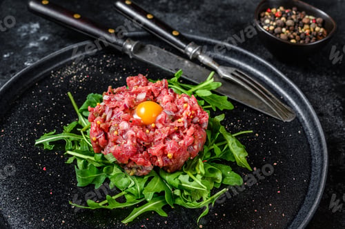 Preview: Beef tartare with arugula and quail egg. Black background. Top view