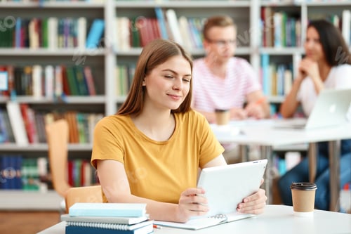 Preview: Young woman working on tablet at table in library