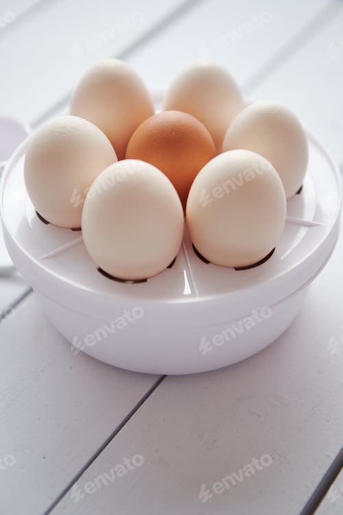 Preview: Chicken eggs in a egg electric cooker on a white wooden table