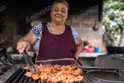 Preview: Latin aged woman cooking meat on a grill