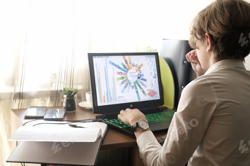 Preview: A young aspiring businessman sits in front of his notebook at his desk and studies the stock market