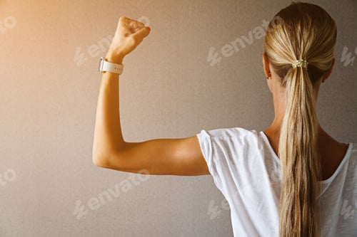 Preview: Young Caucasian woman with blonde hair from behind showing her muscle on hand biceps