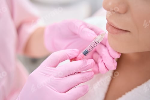 Preview: Doctor injects syringe with cosmetic product into lower lip of patient