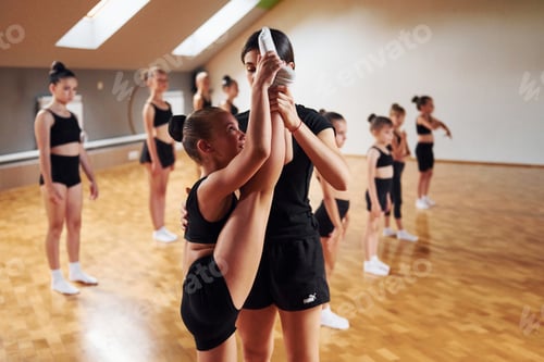 Preview: Coach is helping. Group of female kids practicing athletic exercises together indoors