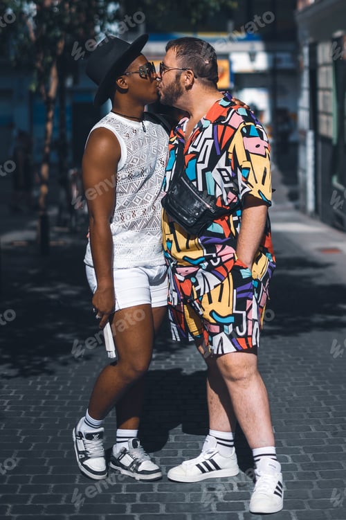 Preview: Portrait of multirracial gay couple with coloured clothes anf fans in the street