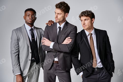 Preview: attractive young interracial friends in smart business suits posing together on gray background