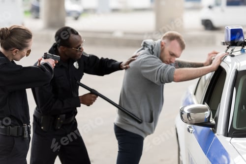 Preview: african american policeman arresting young man and policewoman aiming by handgun