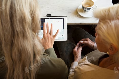 Preview: Mother and daughter sitting together in cafe, looking at digital tablet, rear view