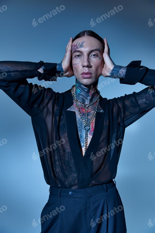 Preview: vertical shot of good looking man in transparent shirt with tattoos touching his head, fashion
