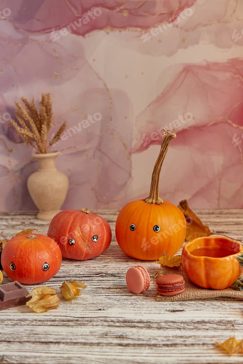 Preview: Cute pumpkins with eyes. Halloween seasonal funny family among macaroons and cup of tea.