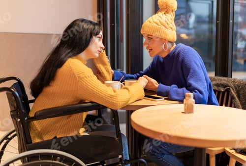 Preview: In a cafeteria, a friend supports the other by holding the hand. She is in a wheelchair recovering.