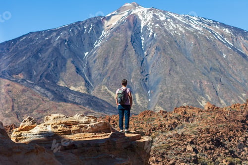 Preview: Back view of traveler man standing on the edge of rock looking to volcano El Teide