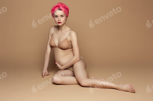 Preview: Young beautiful pregnant woman sitting on brown background