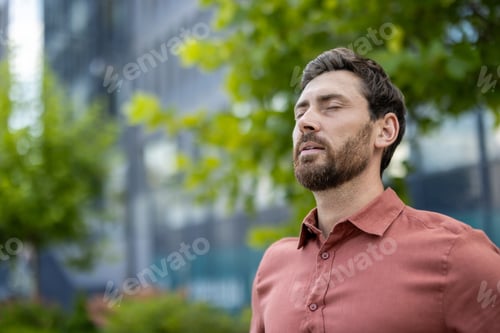 Preview: Relaxed businessman in city street enjoying moment outdoors with eyes closed, feeling peaceful and