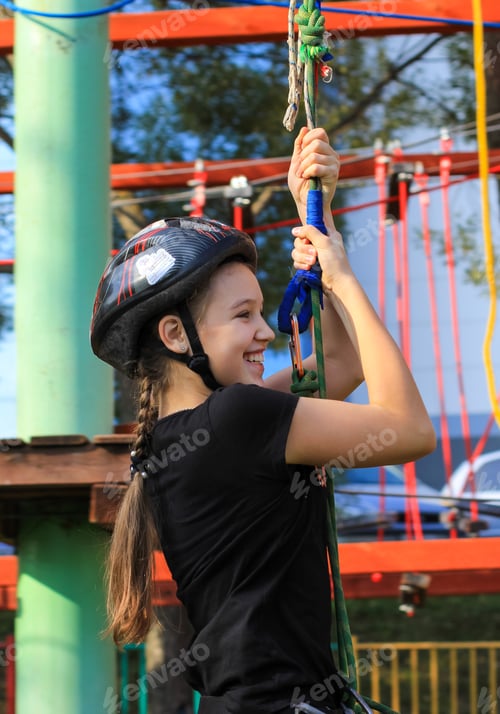 Preview: Girl in safety equipment hiking in the rope park. Climbing adventure park. Sport, outdoor activity.