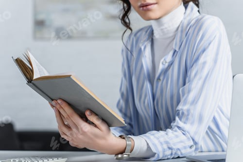 Preview: cropped view of woman studying with book in office