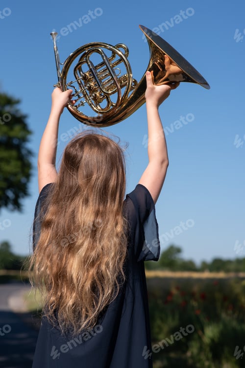 Preview: Teen girl proudly holds her french horn in the sky