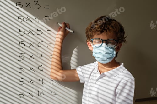 Preview: Schoolboy in mask writing on whiteboard during math lesson