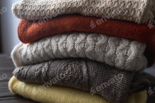 Preview: Folded knitted warm sweaters are stacked. Different knitted patterns. Autumn or winter background.