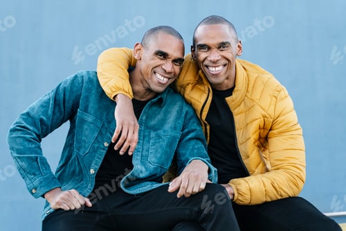 Preview: African American twin brothers smiling and embracing each other, wearing blue and yellow