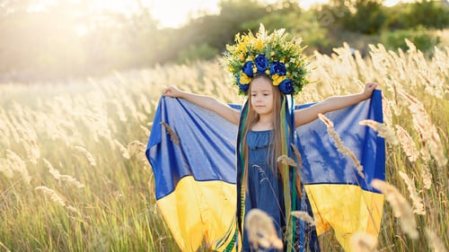 Preview: Girl carries fluttering blue and yellow flag of Ukraine in field.