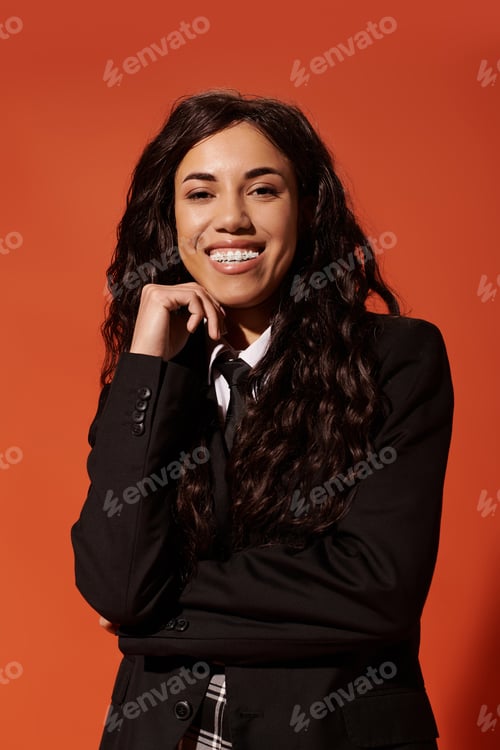Preview: Cheerful young woman with beautiful curls exuding student vibes in striking orange backdrop