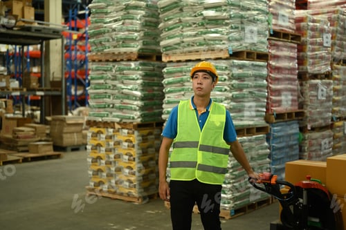 Preview: Male warehouse worker in hardhats and reflective jackets pulling a pallet truck walking.