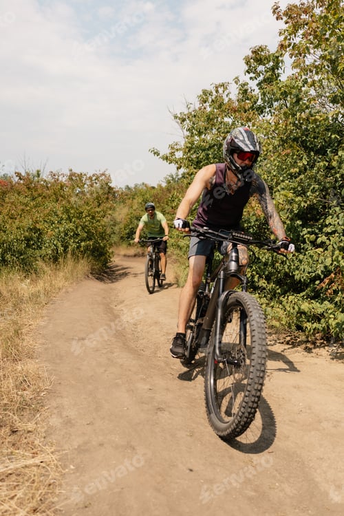 Preview: Two cyclists riding mountain bikes on a dirt trail through lush greenery